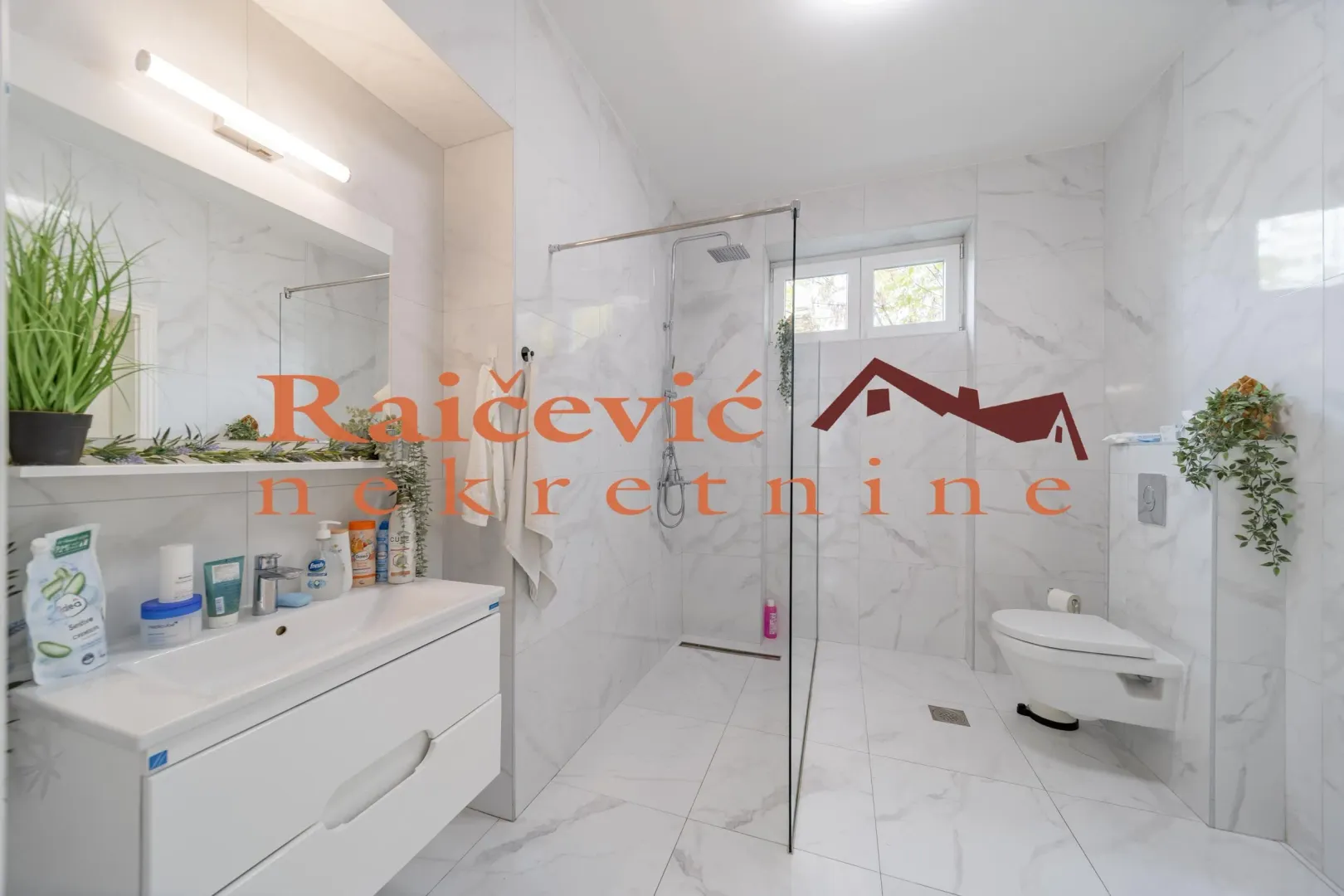 Modern bathroom with white marble tiles, a walk-in shower with glass partition, and a wall-hung toilet.
