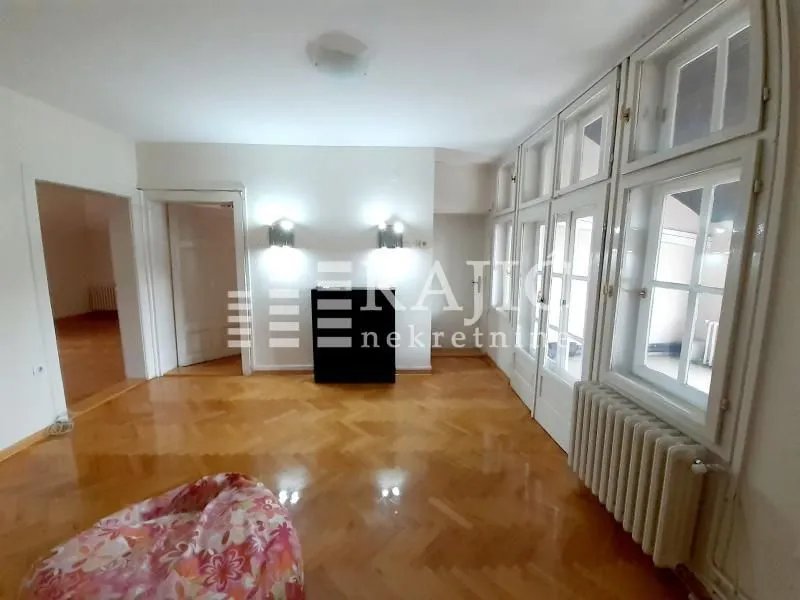 Empty room with parquet flooring and large windows.