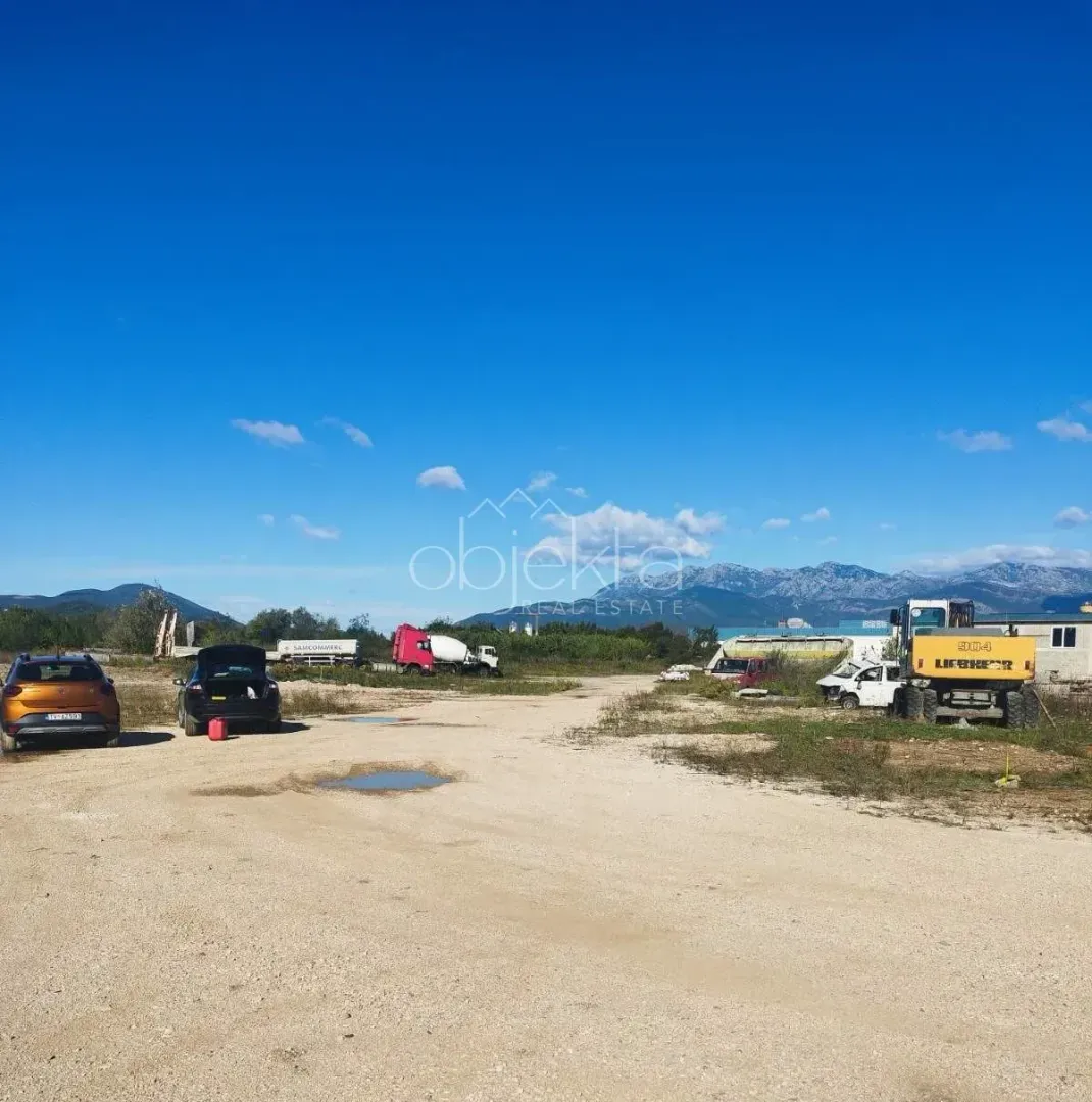 Pogled na otvoreni plac sa parkiranim vozilima i građevinskom mehanizacijom.