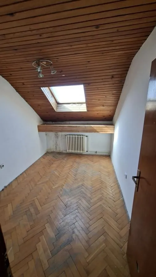 Prazna potkrovna prostorija sa drvenim krovnim prozorom i parketom.