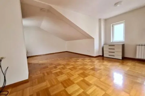 Prazna potkrovna prostorija sa parketom i malom komodom pored prozora. - image 13