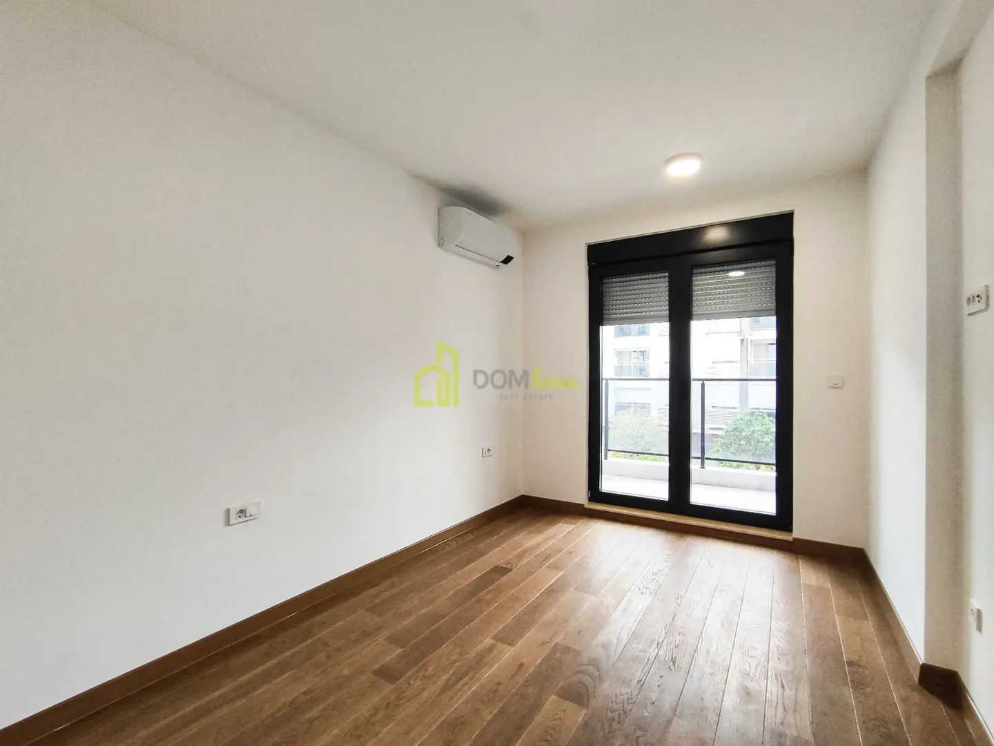 Empty room with wooden flooring, air conditioning unit, and balcony doors.