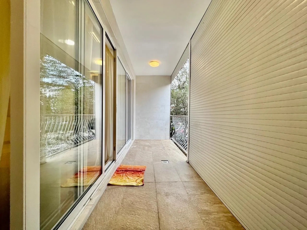 A long and bright balcony with tiled flooring and sliding glass doors.