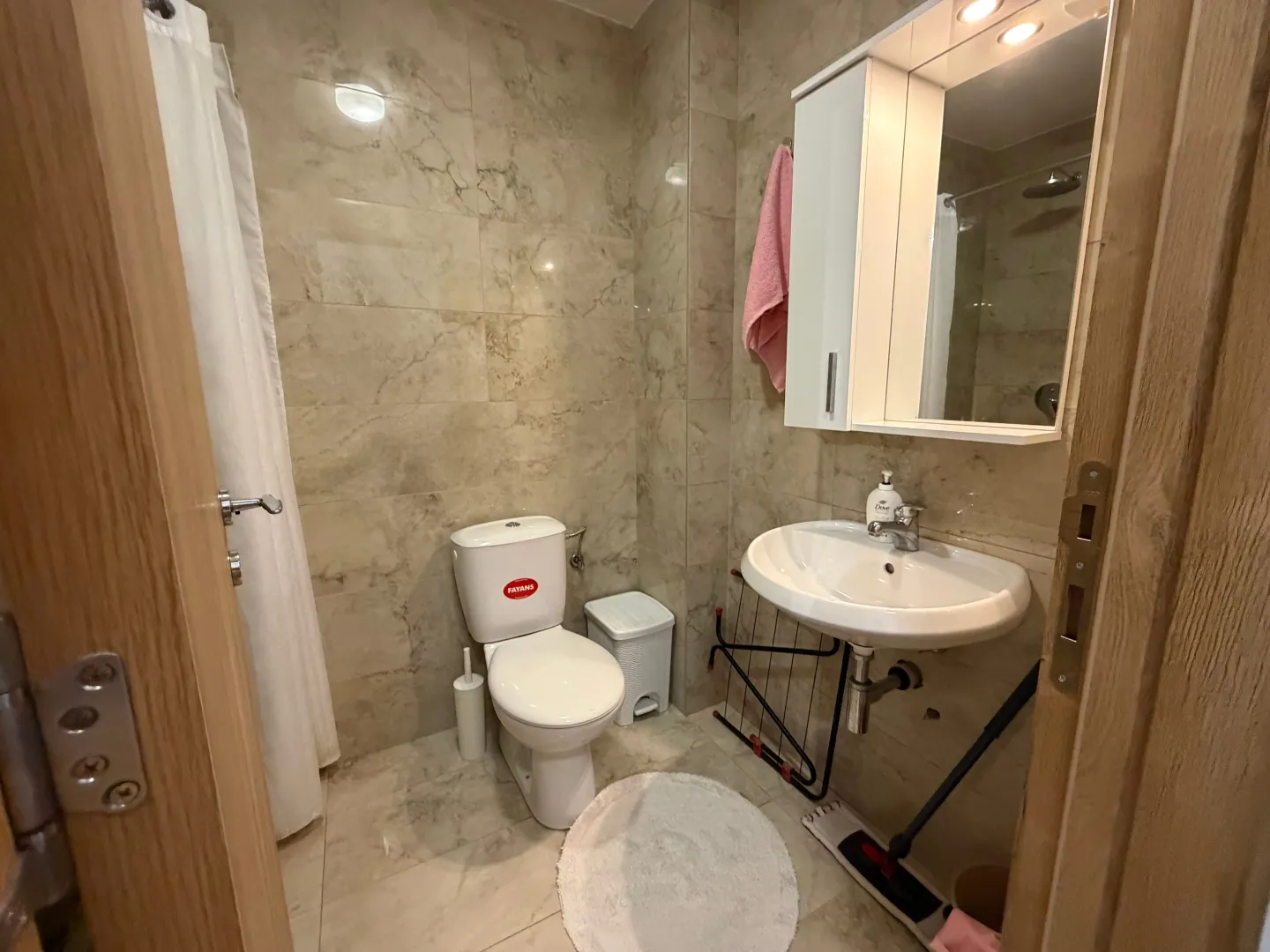 Manje kupatilo sa pločicama, wc šoljom, umivaonikom i ogledalom sa ormarićem.