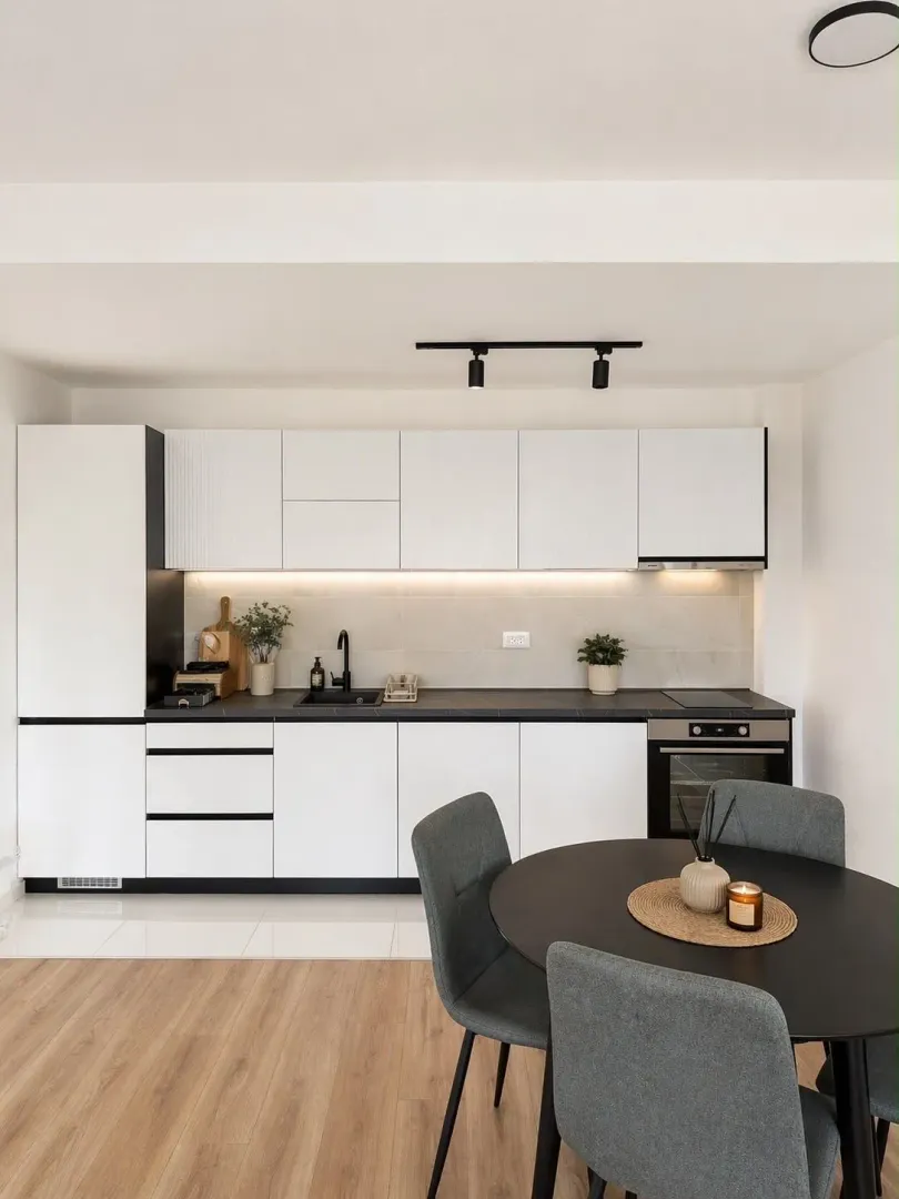 Modern white kitchen with black accents and a dining table.