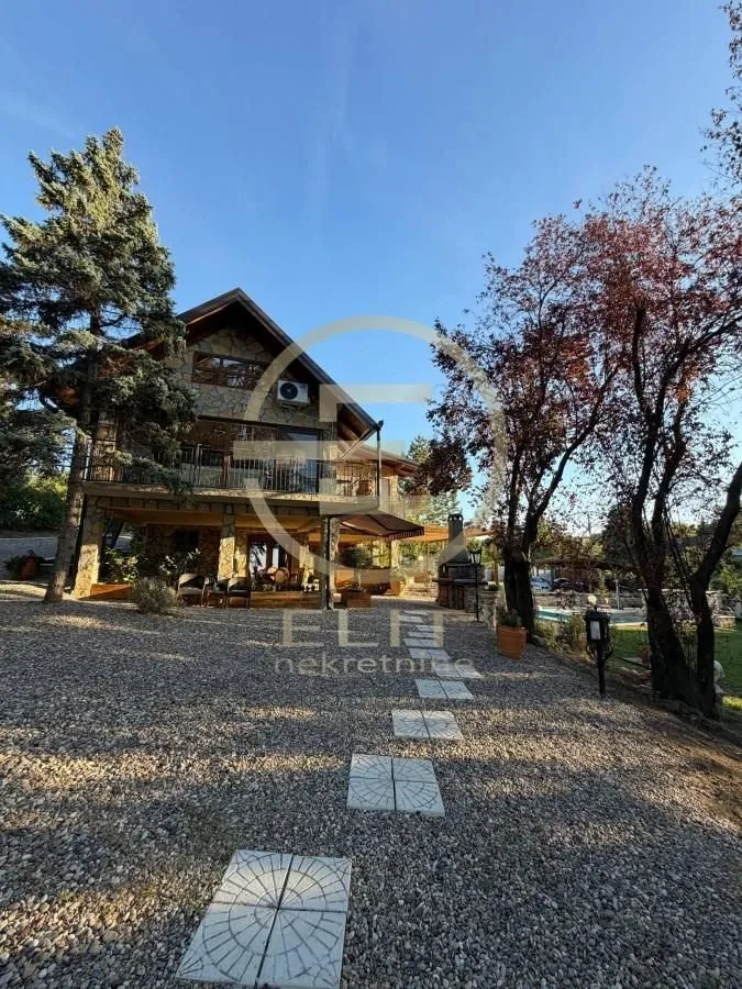Pogled na dvorište i fasadu kuće sa kamenim oblogama i uređenom stazom.