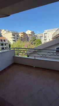 Popločana terasa sa metalnom ogradom i pogledom na grad. - image 2