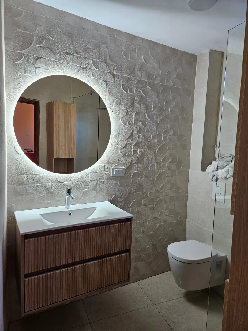 Modern bathroom with a vanity sink, round backlit mirror, and a wall-mounted toilet.