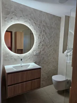 Modern bathroom with a vanity sink, round backlit mirror, and a wall-mounted toilet. - image 5