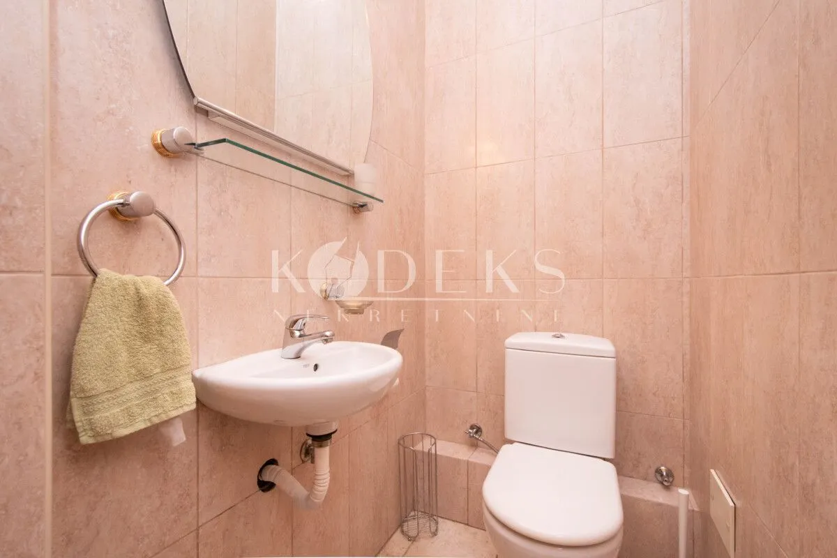 Small bathroom lined with beige tiles featuring a washbasin and a toilet.