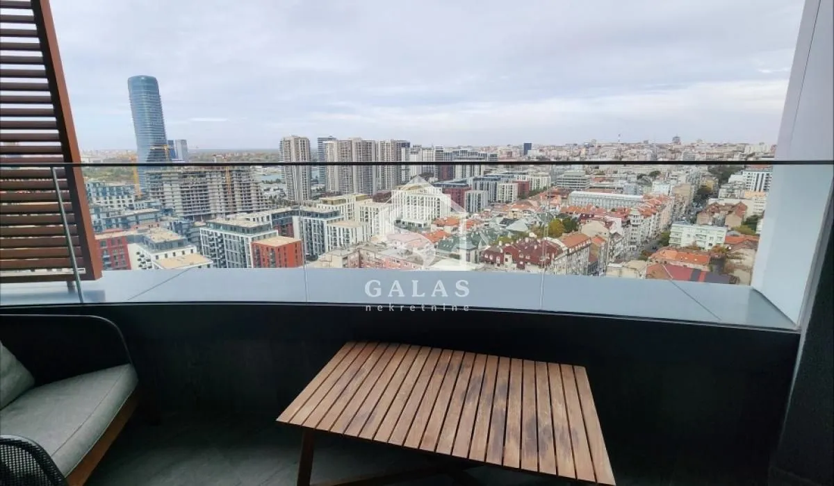 City view from a balcony furnished with a table and an armchair.