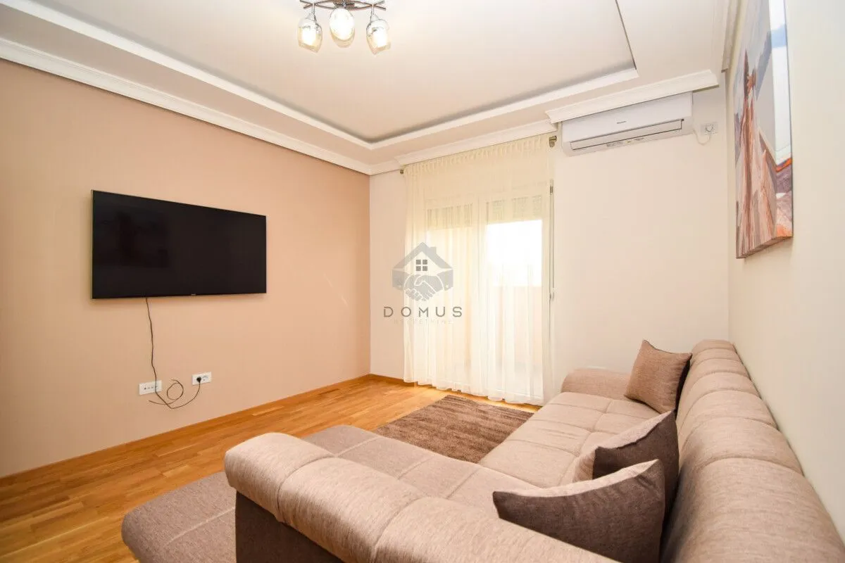 Living room with a corner sofa, wall-mounted television and air conditioning unit.