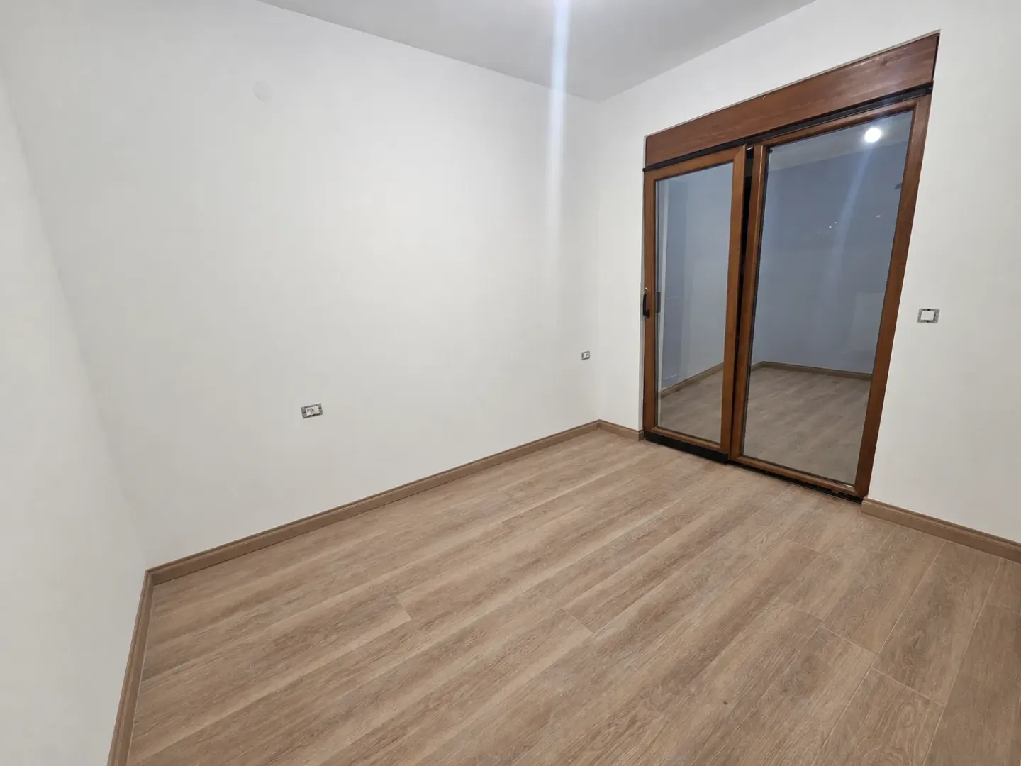 Prazna soba sa laminatom i balkonskim vratima.