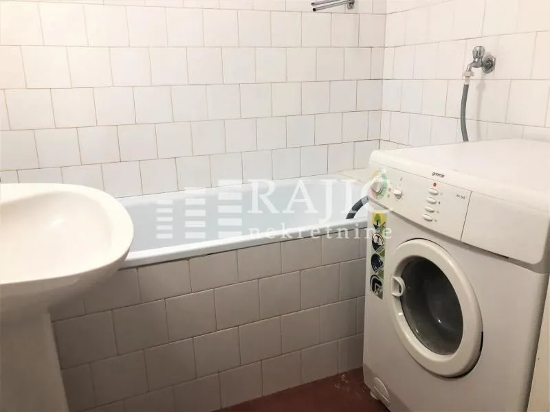 Smaller bathroom with a bathtub, washbasin, and washing machine.