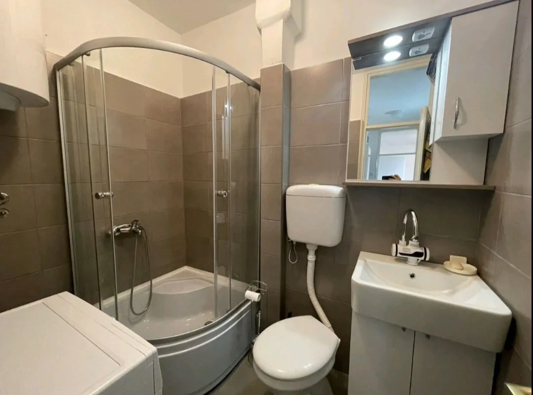 Kompaktno kupatilo sa tuš kabinom, umivaonikom i wc šoljom obloženo braon pločicama.