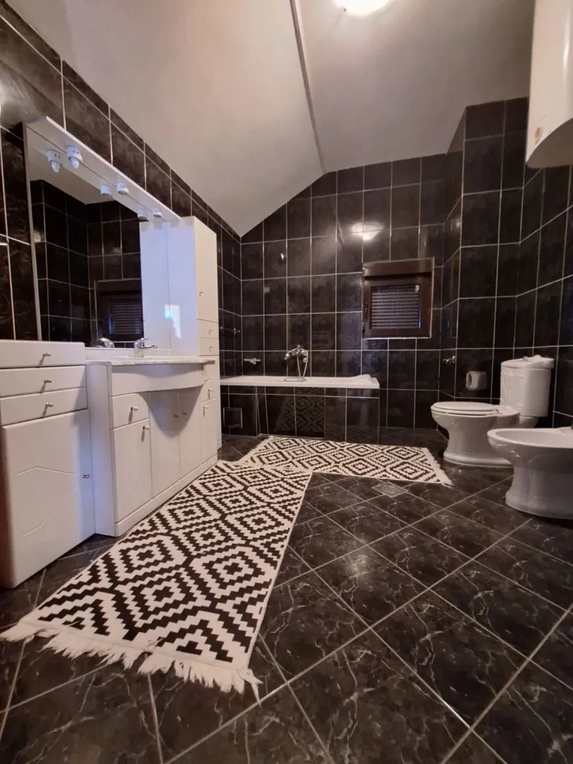 Spacious bathroom featuring dark tiles, a bathtub, sanitary ware, and white bathroom furniture.