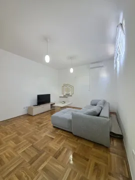 Dnevna soba sa sivom ugaonom garniturom, televizorom i drvenim podom. - image 2