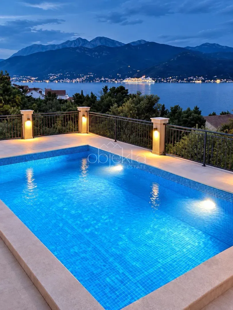 Illuminated swimming pool with sea and mountain views at dusk.