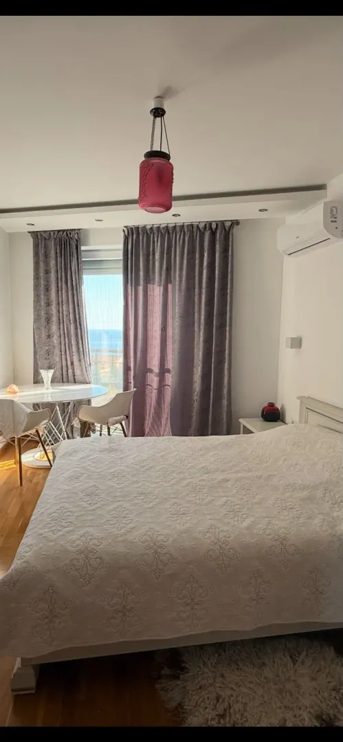 Spavaća soba sa bračnim krevetom, trpezarijskim stolom kod prozora i pogledom na more.