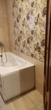 A bathroom featuring a bathtub and floral-patterned wall tiles. - image 6
