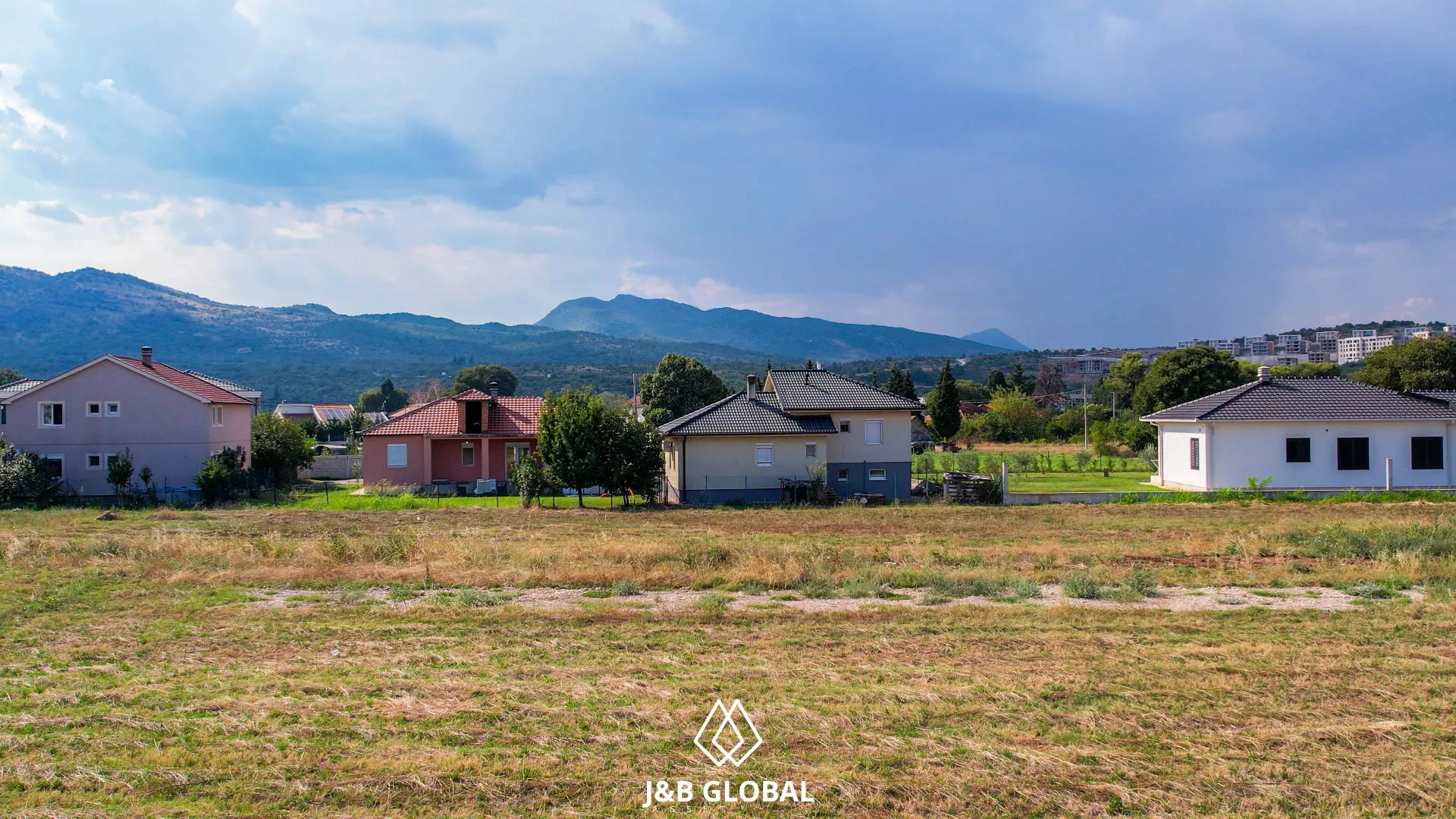 Pogled na kuće i okolni pejzaž sa brdima u pozadini.