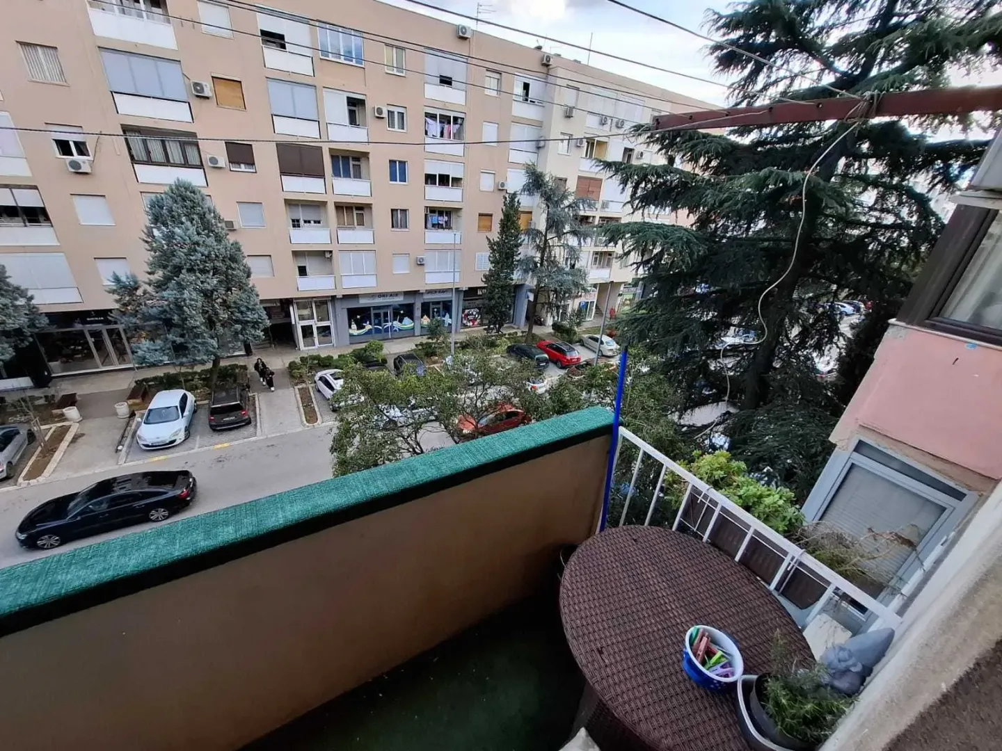 Pogled sa balkona na ulicu, parking i okolne zgrade.