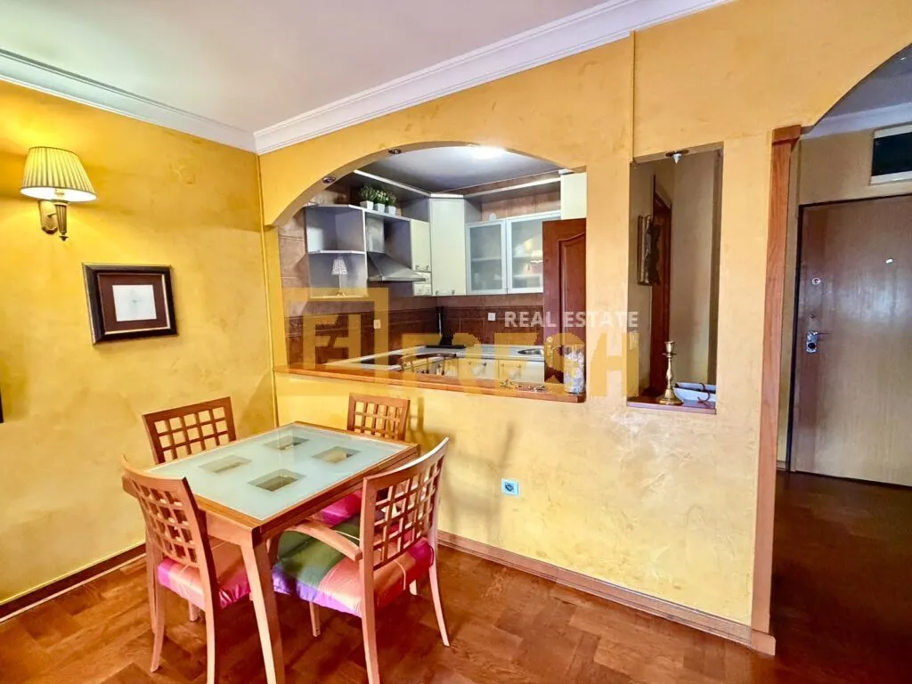 Dining area with a wooden table and chairs, overlooking the kitchen through a pass-through window.