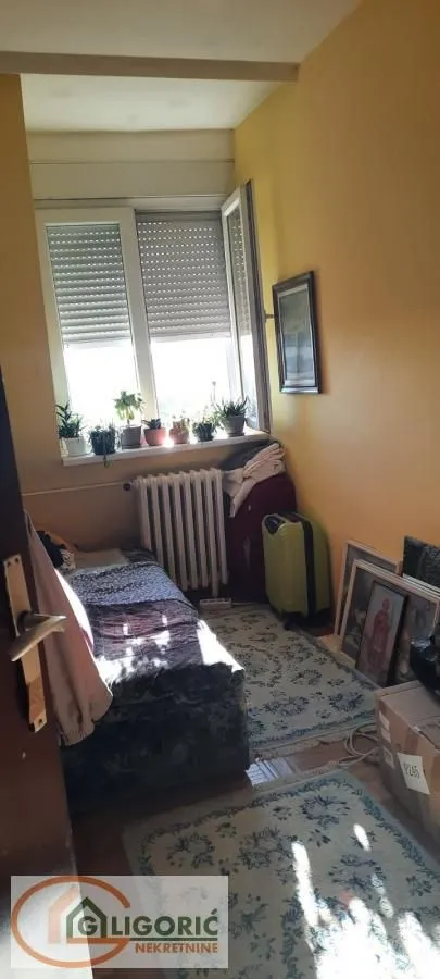 Manja spavaća soba sa krevetom, prozorom i ličnim stvarima.
