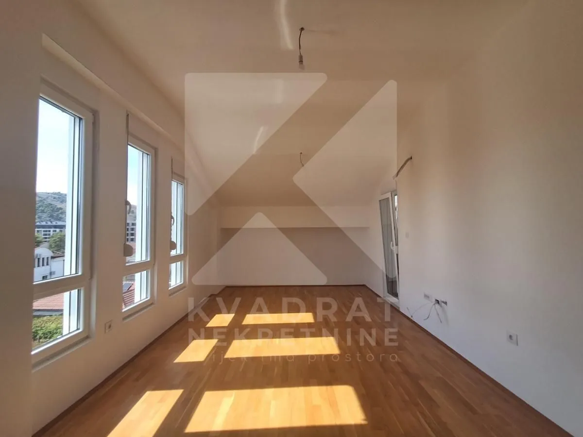 Empty room with hardwood floors and multiple windows.