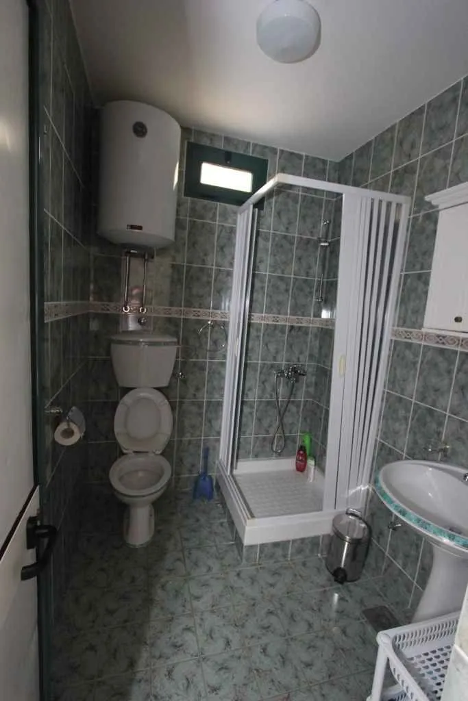 Jednostavno kupatilo sa tuš kabinom i sivo-zelenim pločicama.