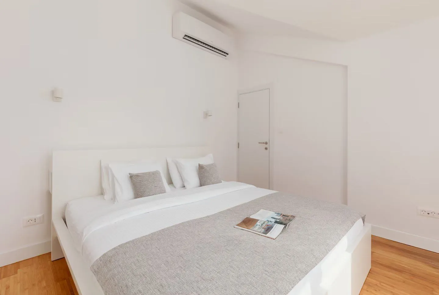 Bright bedroom with a white bed and an air conditioning unit on the wall.