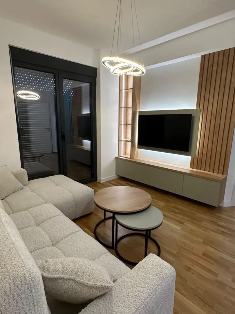 Moderna i svijetla dnevna soba sa ugaonom garniturom, televizorom i drvenim detaljima.