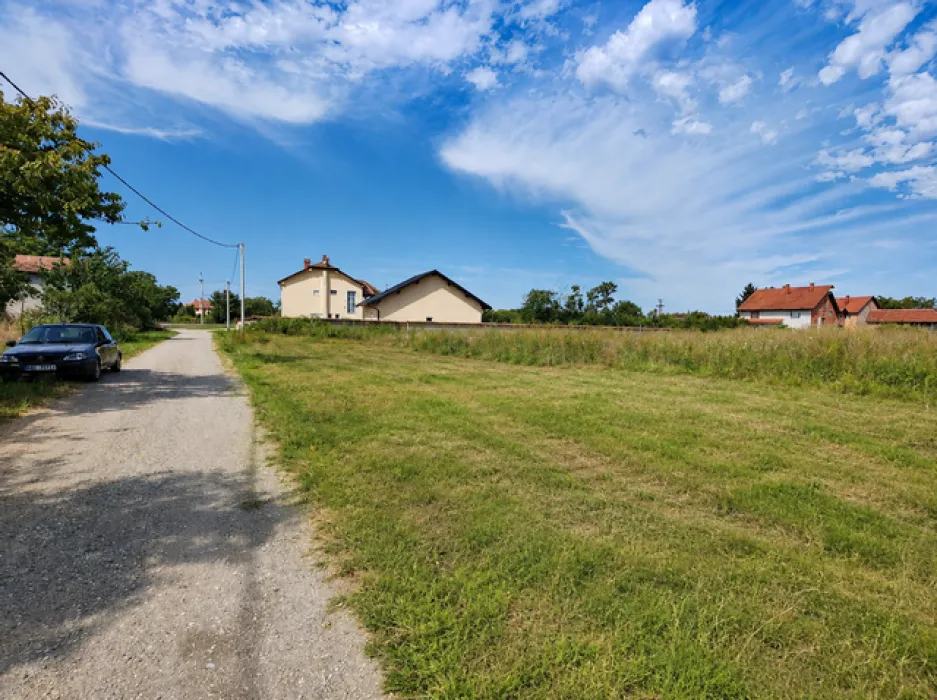 Zemljište pored seoskog puta sa kućama u pozadini.