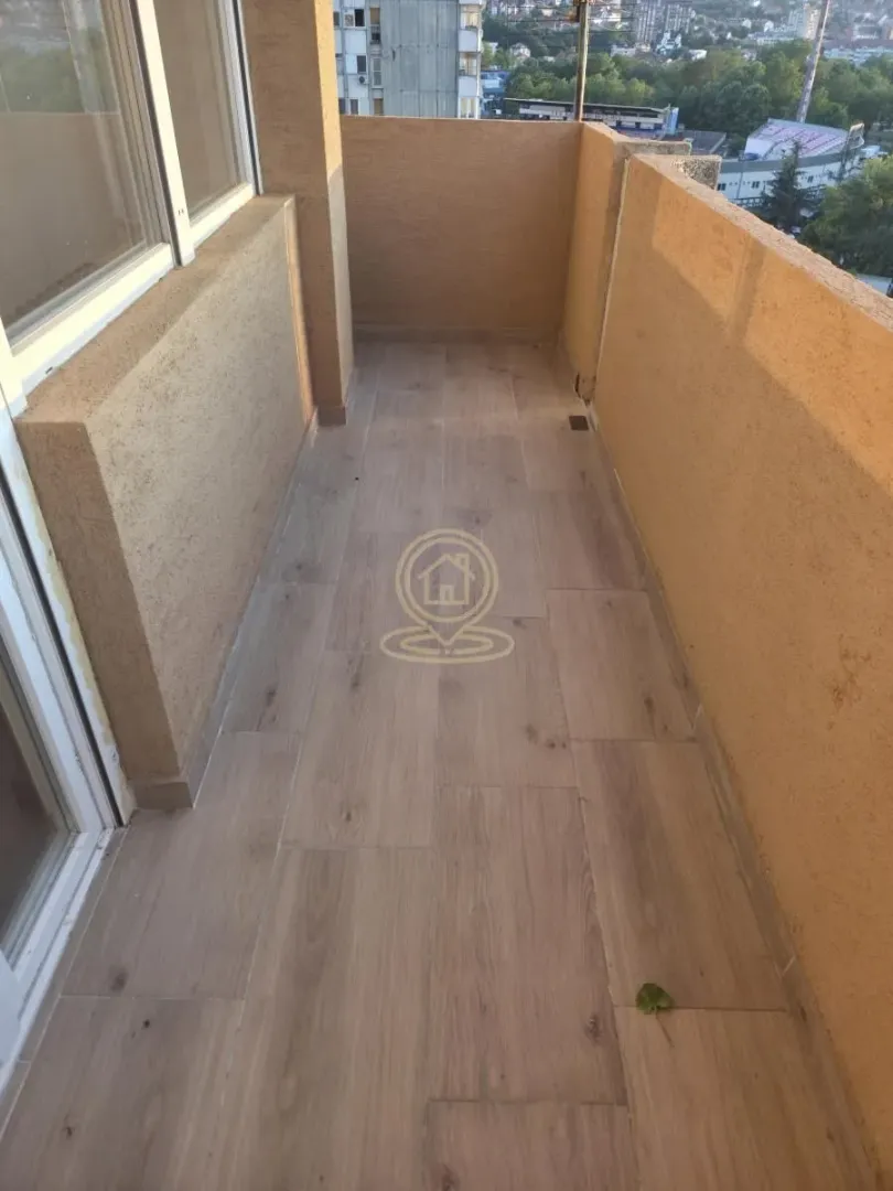 Prazan balkon sa podom u imitaciji drveta i bež zidovima.