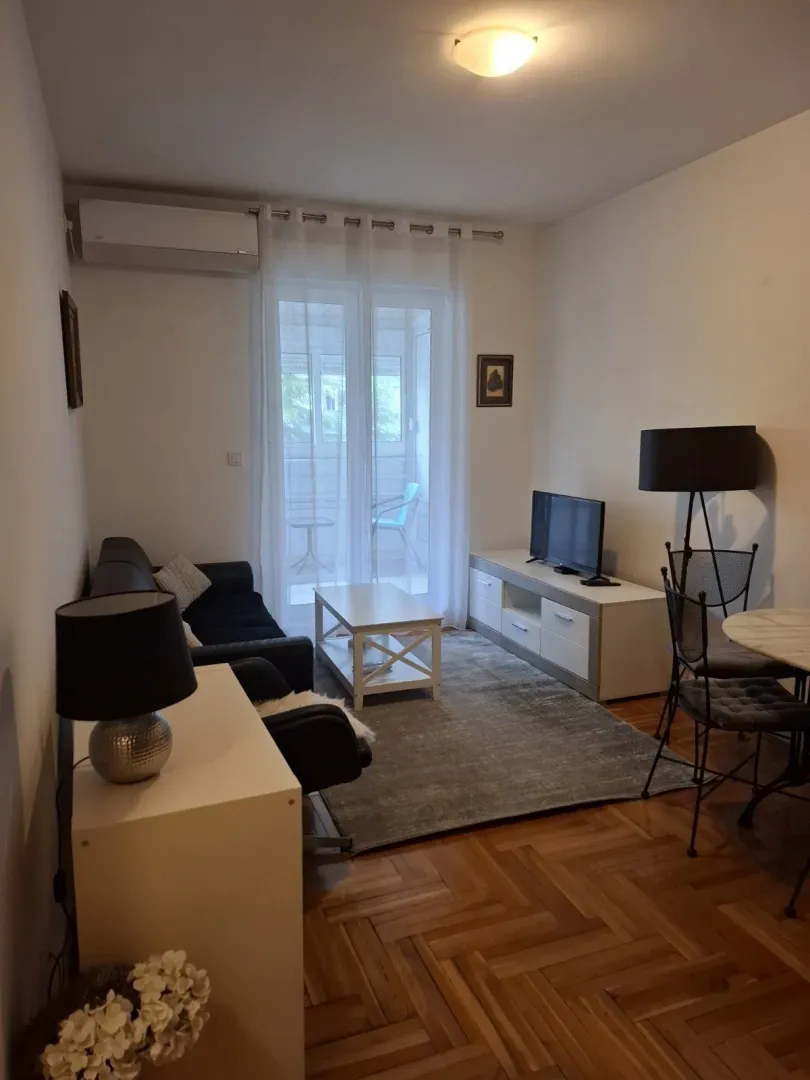Svijetla dnevna soba sa garniturom za sjedenje, televizorom i izlazom na balkon.