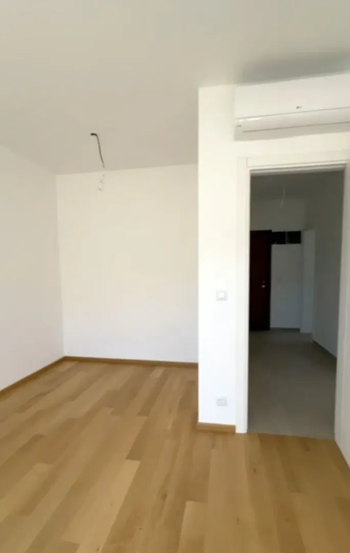 Prazna soba sa drvenim podom i klima uređajem na zidu.