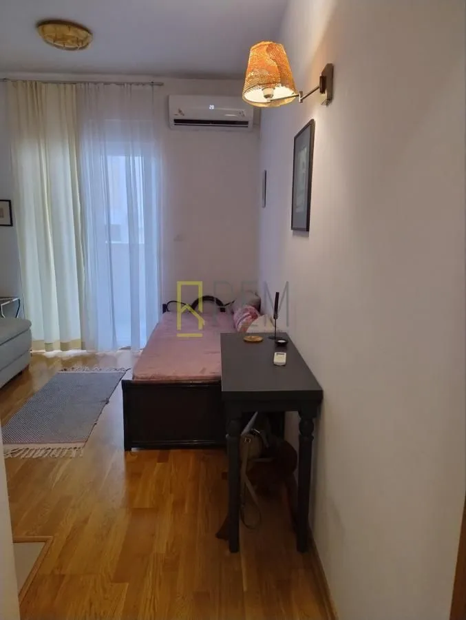 Manja spavaća soba sa krevetom, radnim stolom i izlazom na terasu.