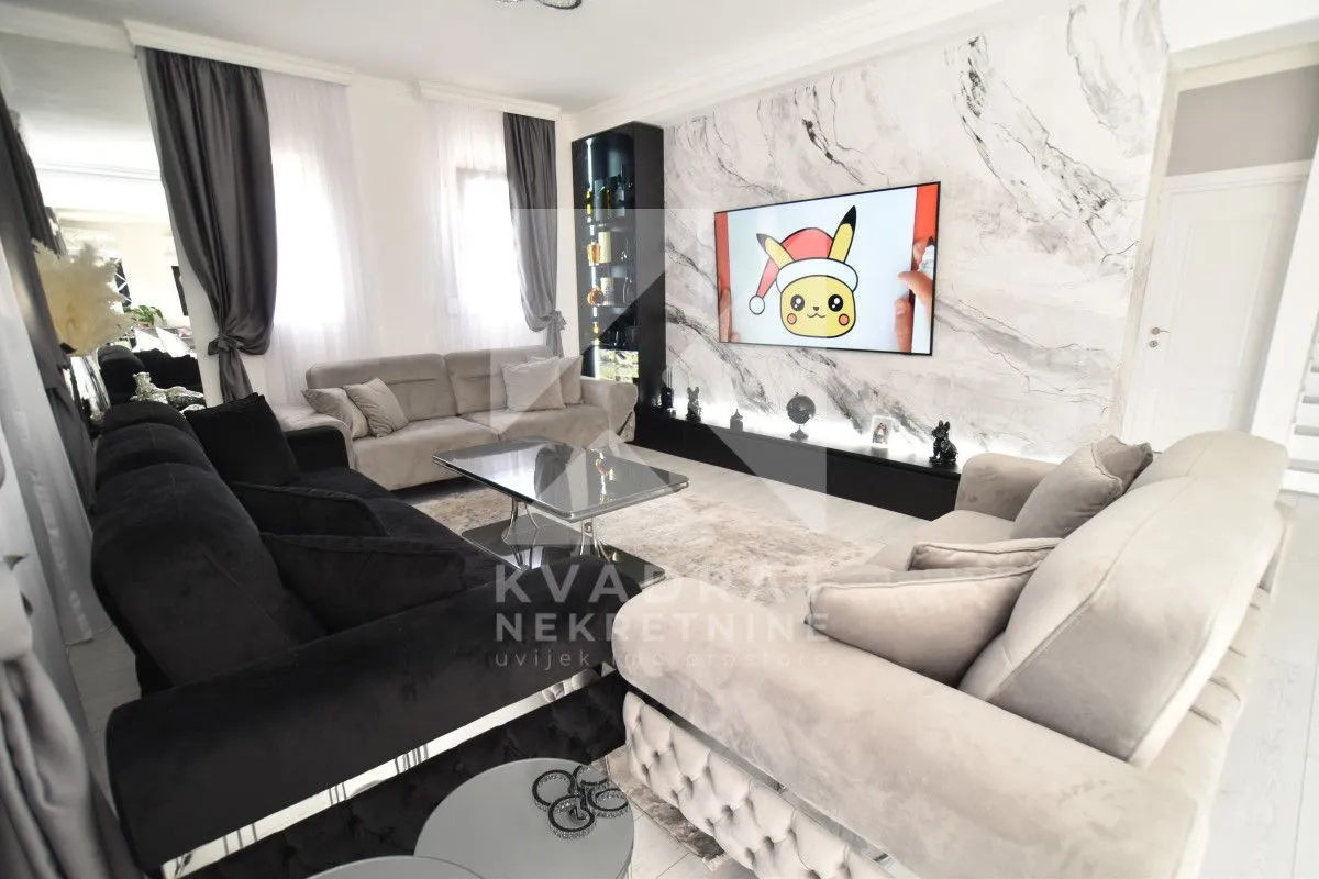 Modern living room with a sofa set, coffee table, and TV on a marble-clad wall.