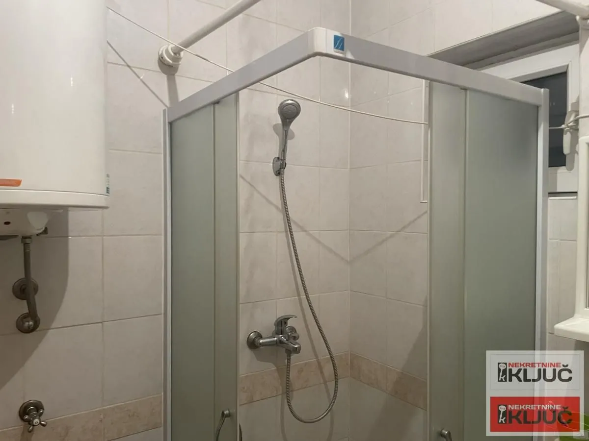 Pogled na tuš kabinu i bojler u kupatilu.