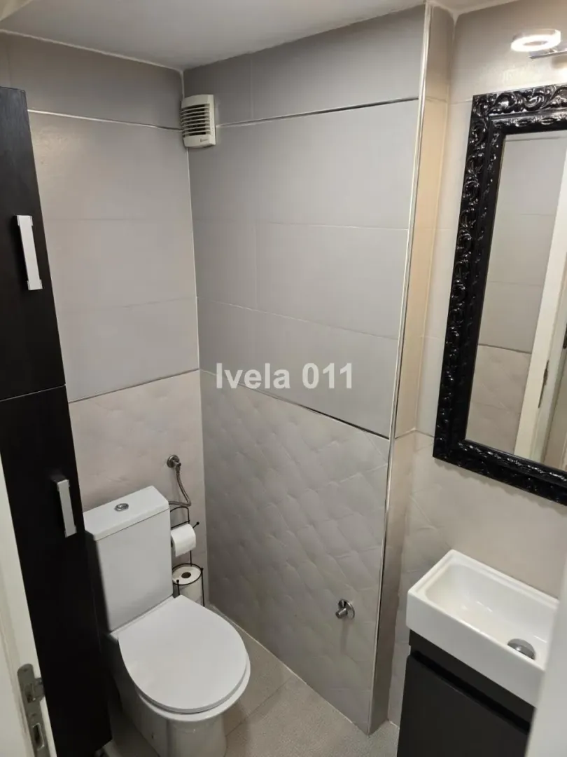 Manje kupatilo sa sivim pločicama, WC šoljom i umivaonikom sa ogledalom.