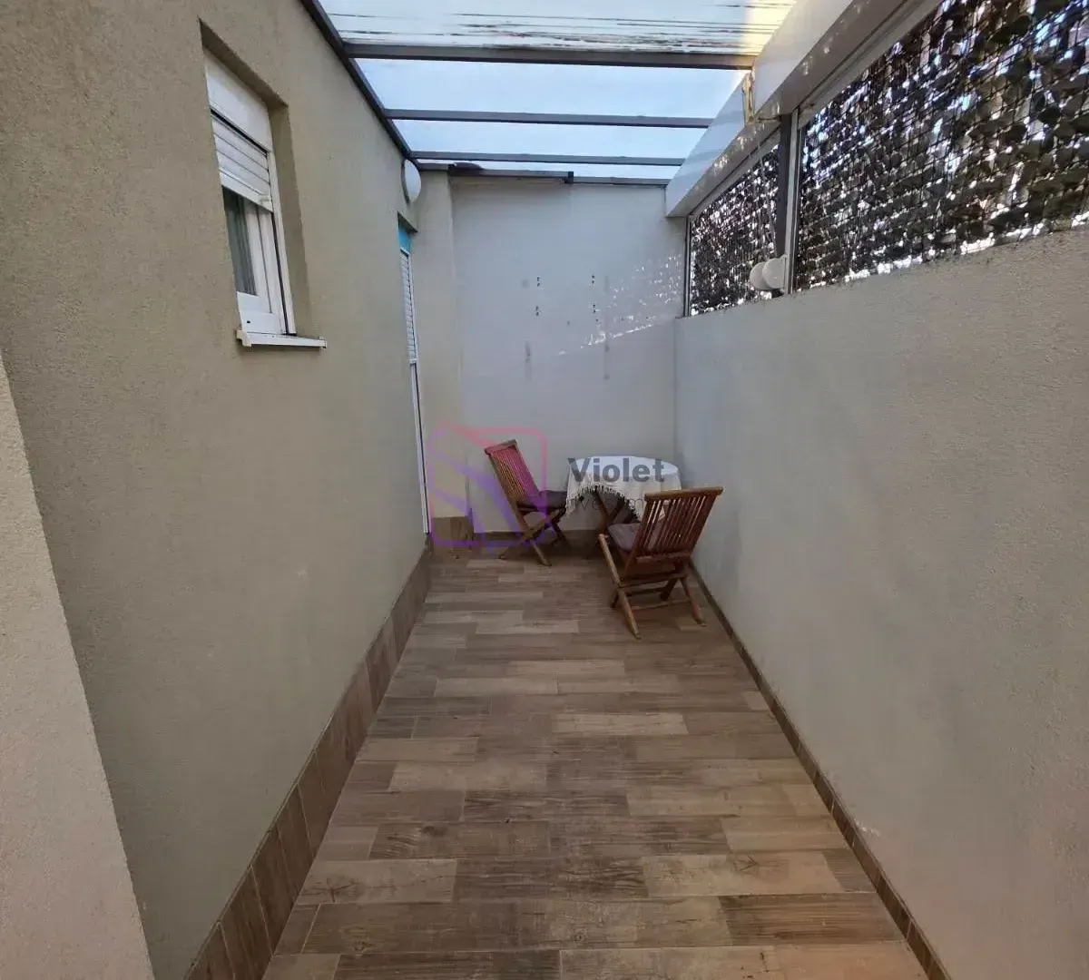 Covered terrace with a table and two wooden chairs.