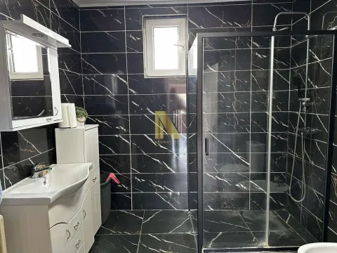 Kupatilo obloženo tamnim pločicama sa tuš kabinom i umivaonikom. - image 12