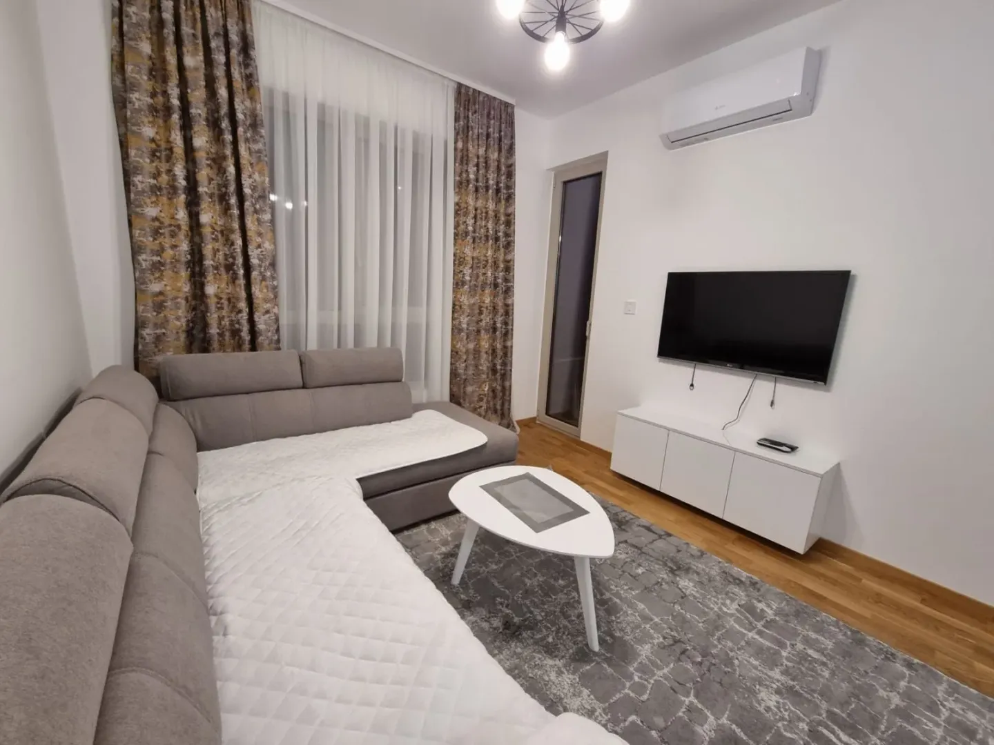 Living room with a sectional sofa, TV, and air conditioning unit.