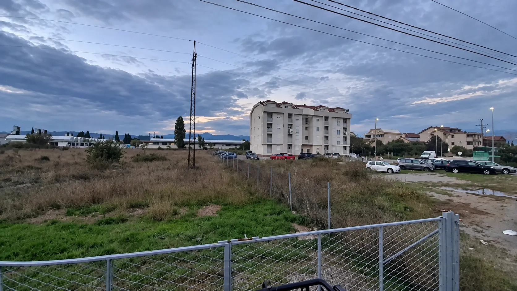 Pogled na višestambenu zgradu i okolno neizgrađeno zemljište u sumrak.
