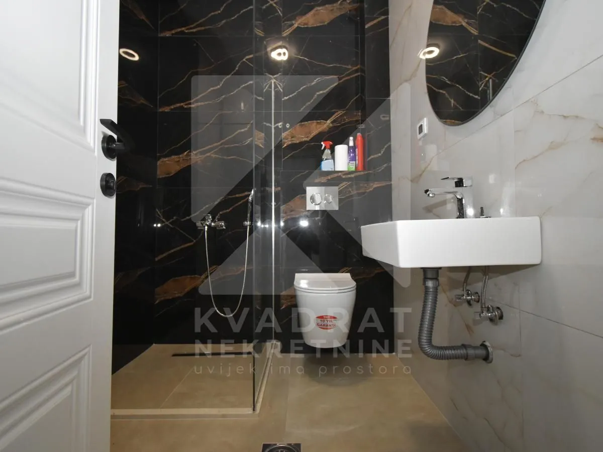 Modern bathroom with a walk-in shower, washbasin, and wall-mounted toilet.