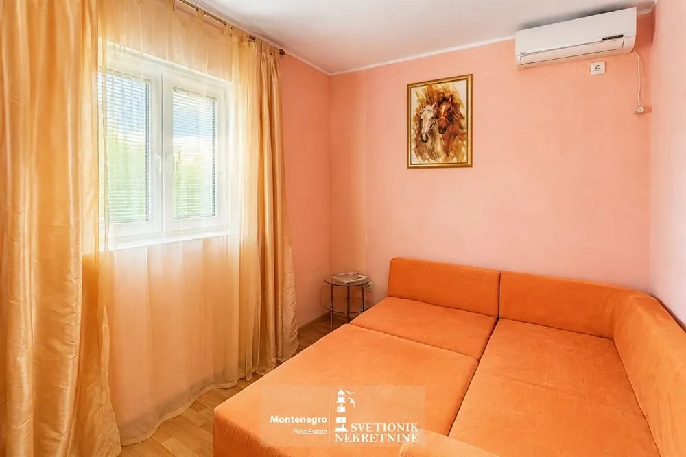 Manja spavaća soba sa narandžastim krevetom, prozorom sa žutim zavesama i klima uređajem.