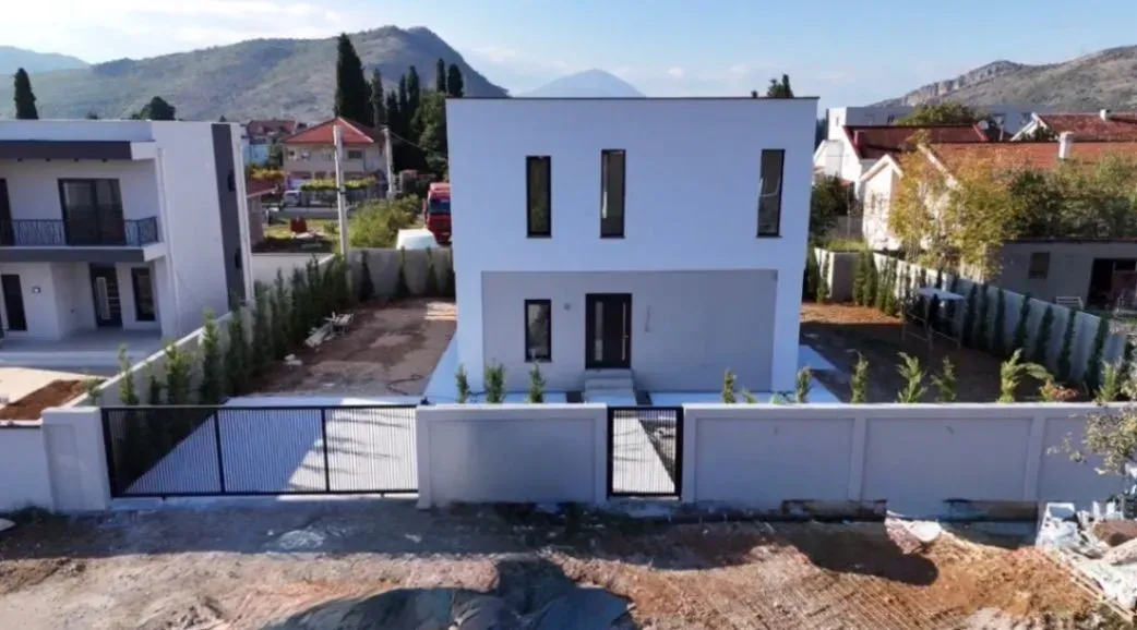 Prednji pogled na dvorište i fasadu moderne kuće sa ogradom.