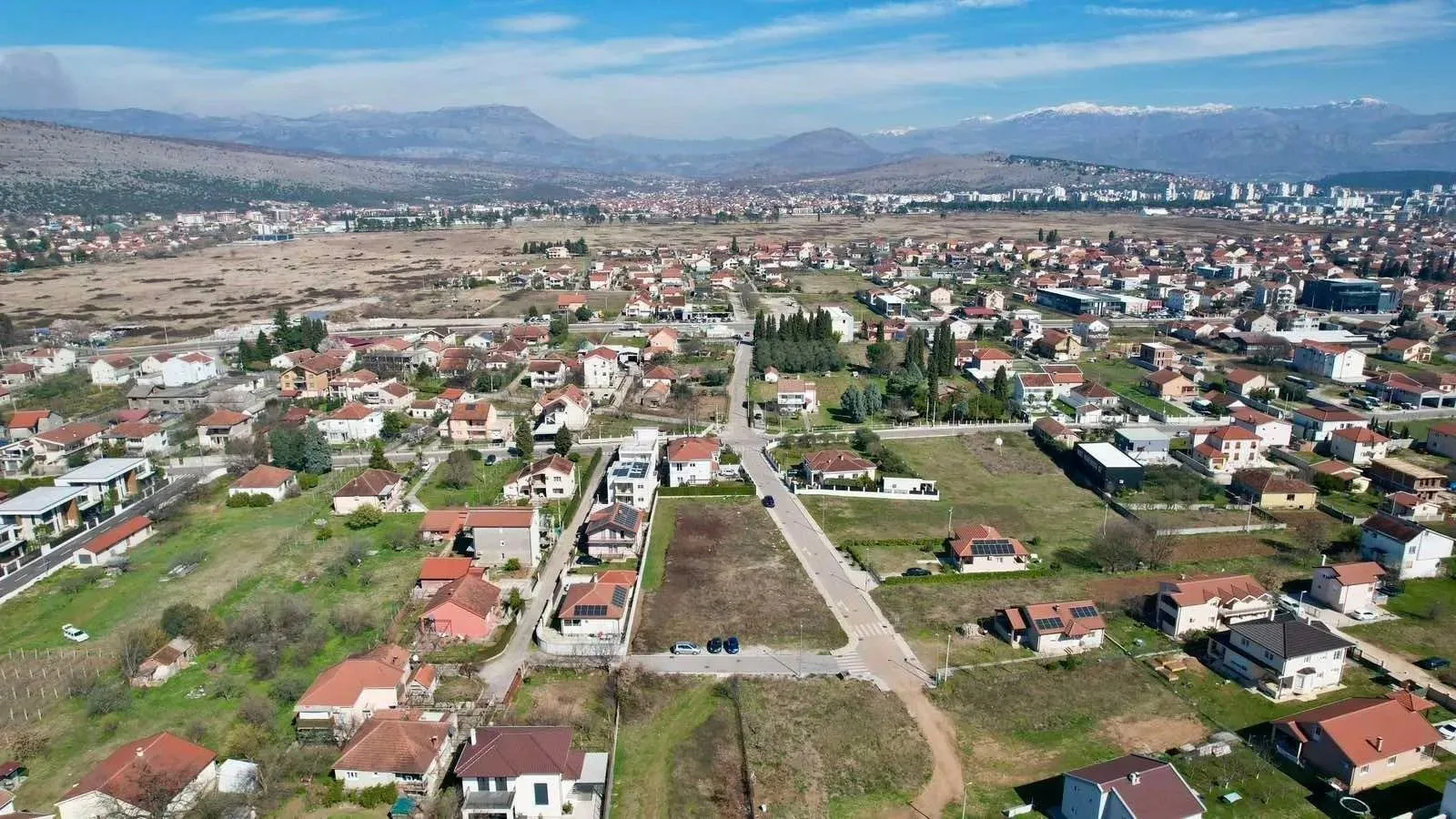 Pogled iz vazduha na prigradsko naselje sa kućama i planinama u pozadini.