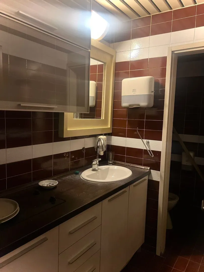 Bathroom with a vanity, cabinetry, and brown and white tiled walls.