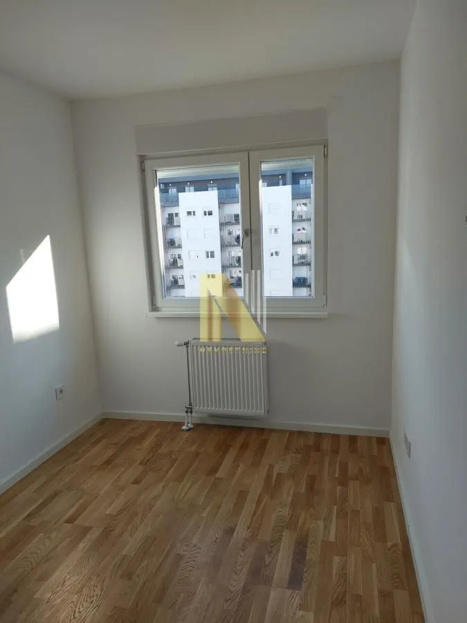 Prazna soba sa parketom i prozorom koji gleda na susednu zgradu.